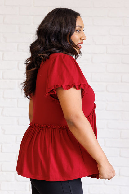 Woman wearing a red blouse with ruffled sleeves against a white brick wall.