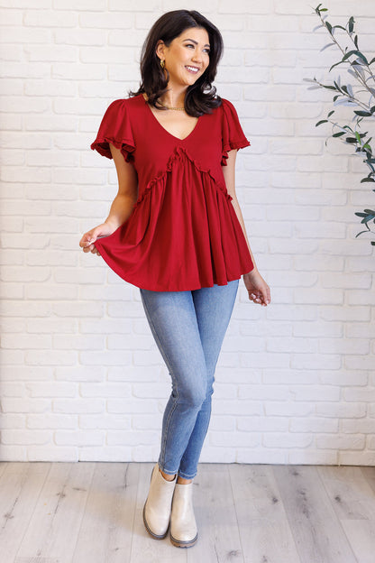 Woman wearing a red blouse and blue jeans standing against a white brick wall.