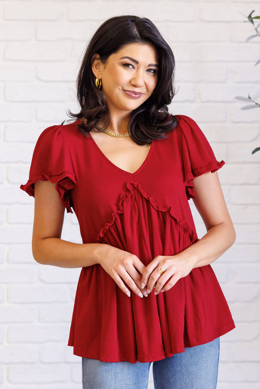 Woman wearing a red blouse with ruffled details against a white brick wall.