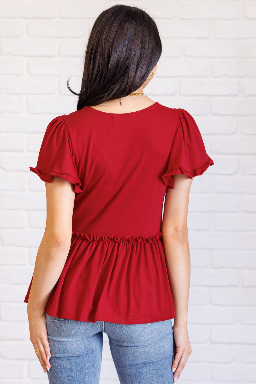 Red blouse with ruffled sleeves worn by a person against a white brick wall.