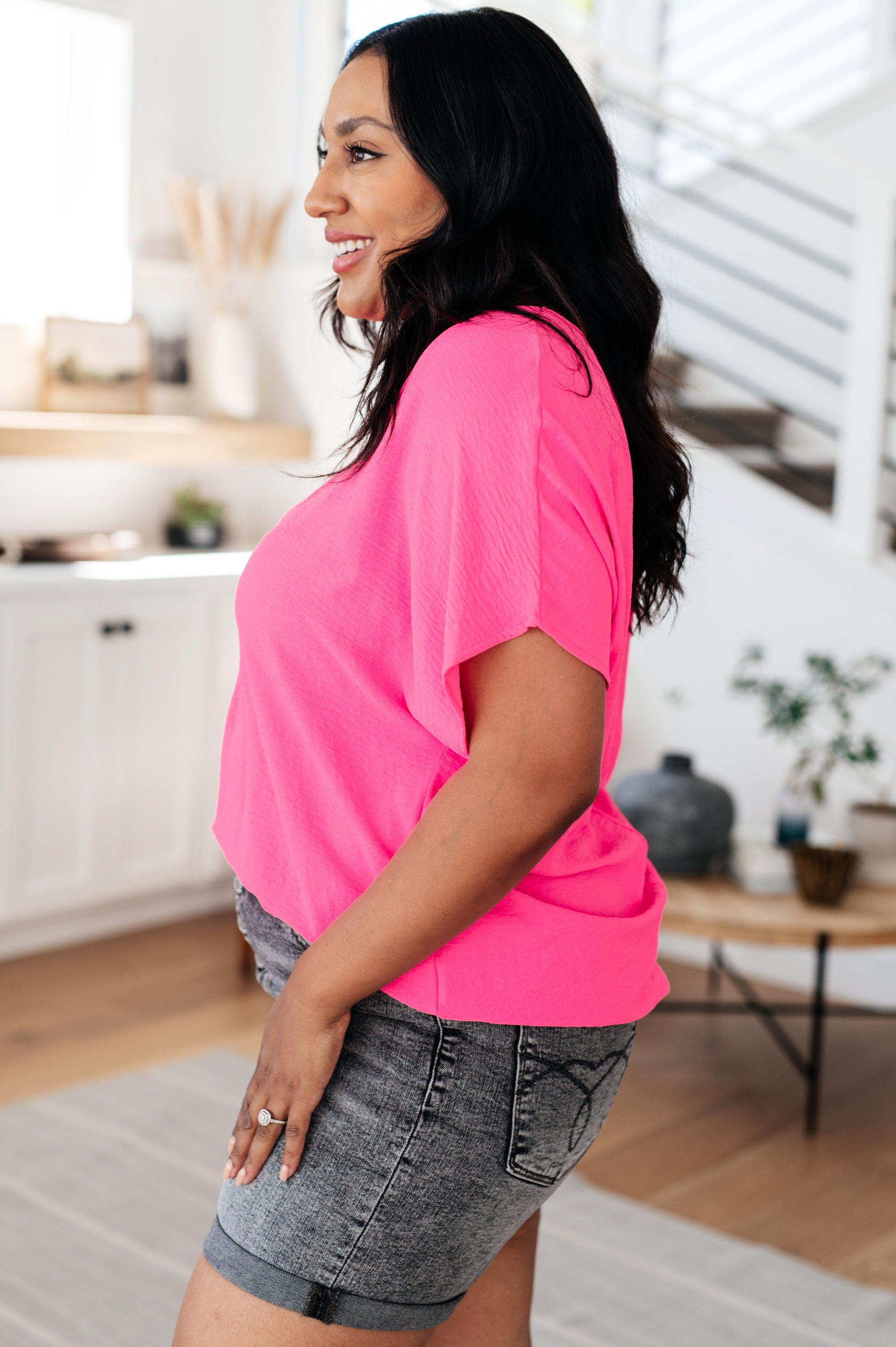 Woman wearing a bright pink shirt and gray shorts in a home setting