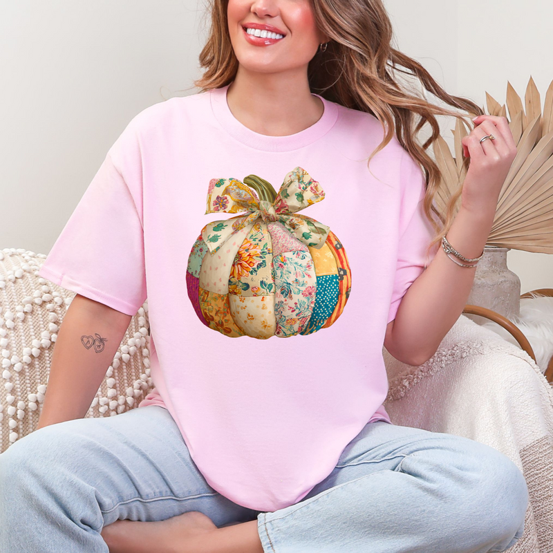 Woman wearing a pink t-shirt with a colorful pumpkin design, sitting on a couch.