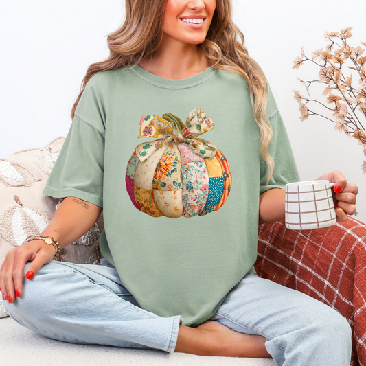Woman wearing a green t-shirt with a patchwork pumpkin design, sitting on a couch holding a mug.