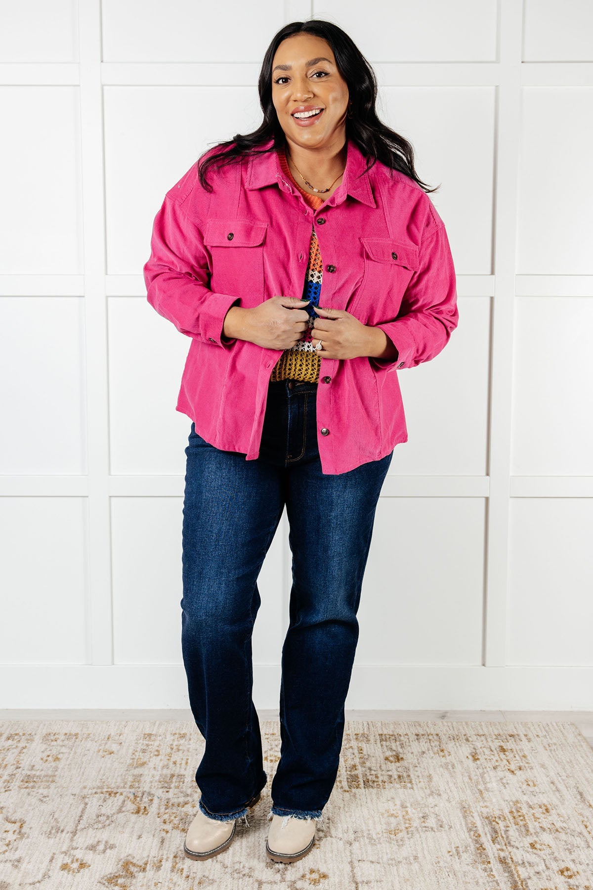 Person wearing a pink jacket and blue jeans standing against a white paneled wall.