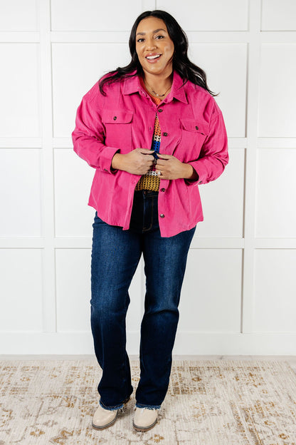 Person wearing a pink jacket and blue jeans standing against a white paneled wall.