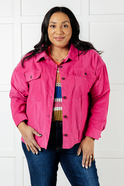 Woman wearing a bright pink jacket over a colorful shirt with a white background
