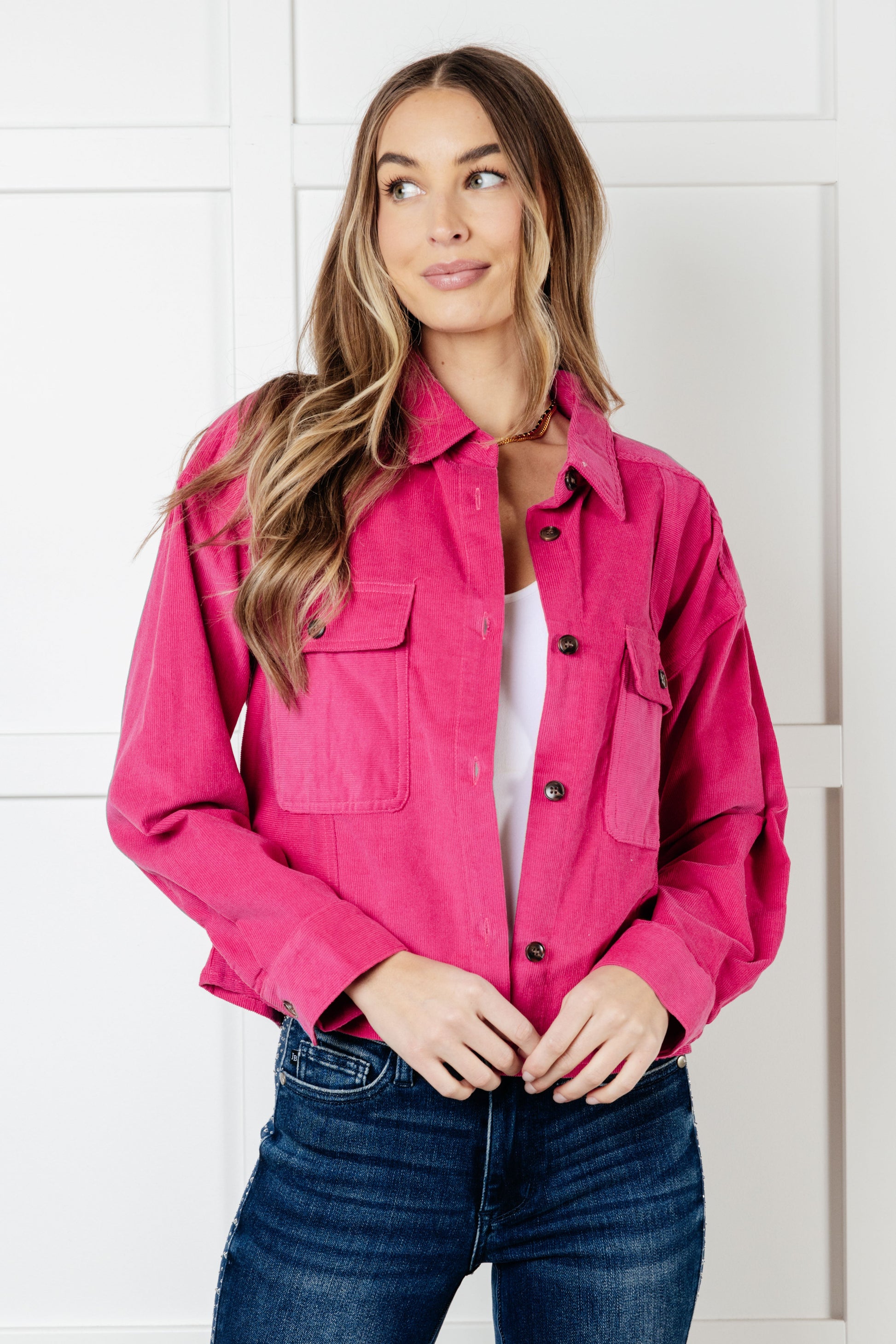 Woman wearing a bright pink jacket and blue jeans against a white background