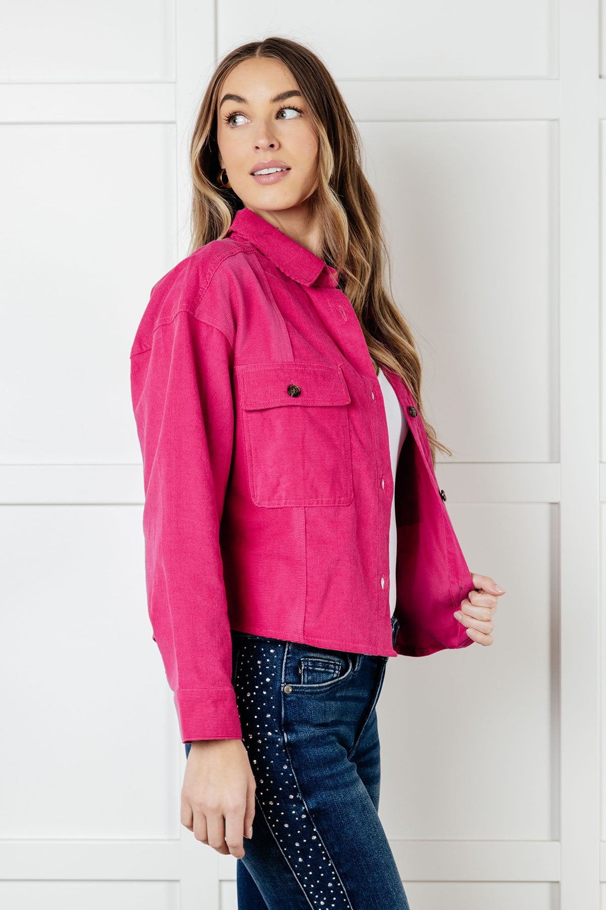 Woman wearing a bright pink jacket and blue jeans against a white background