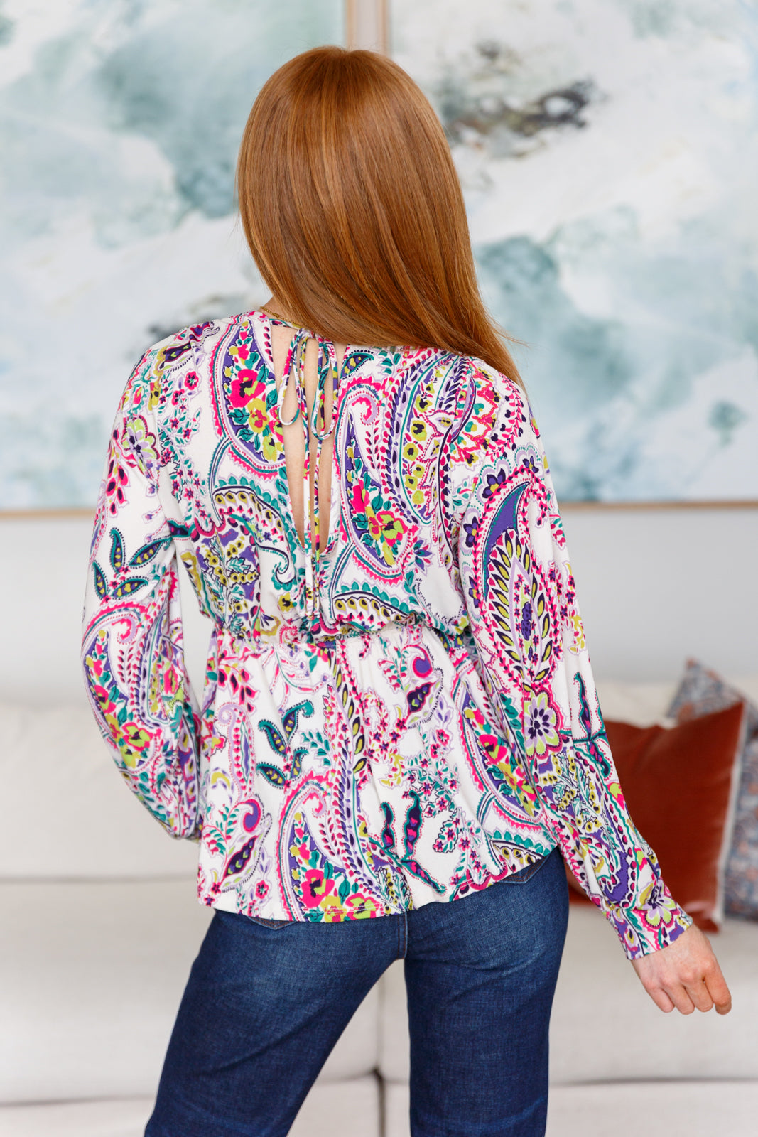 Woman wearing a colorful paisley blouse sitting on a couch.