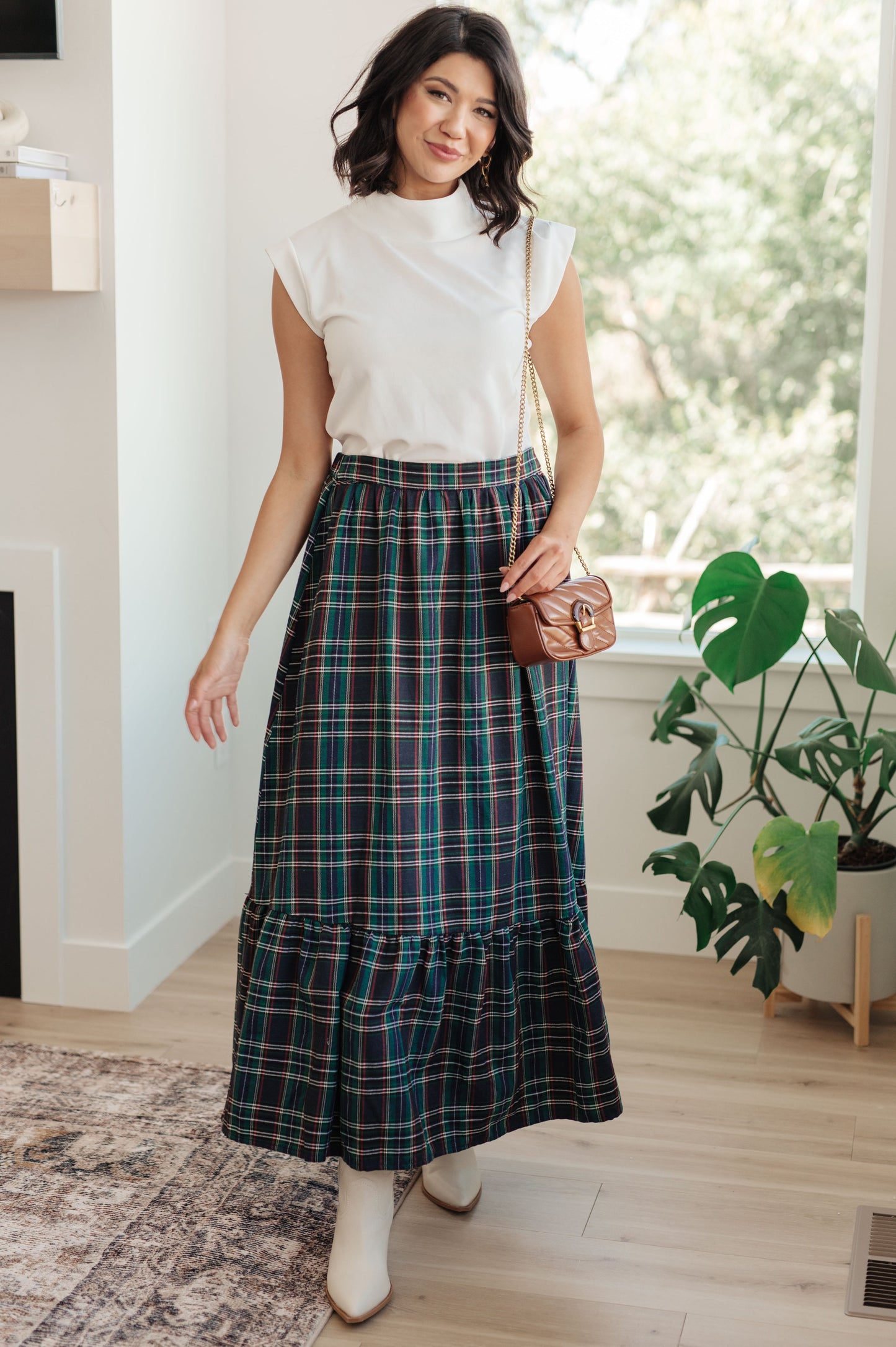Woman wearing a white top and plaid skirt indoors with a plant in the background