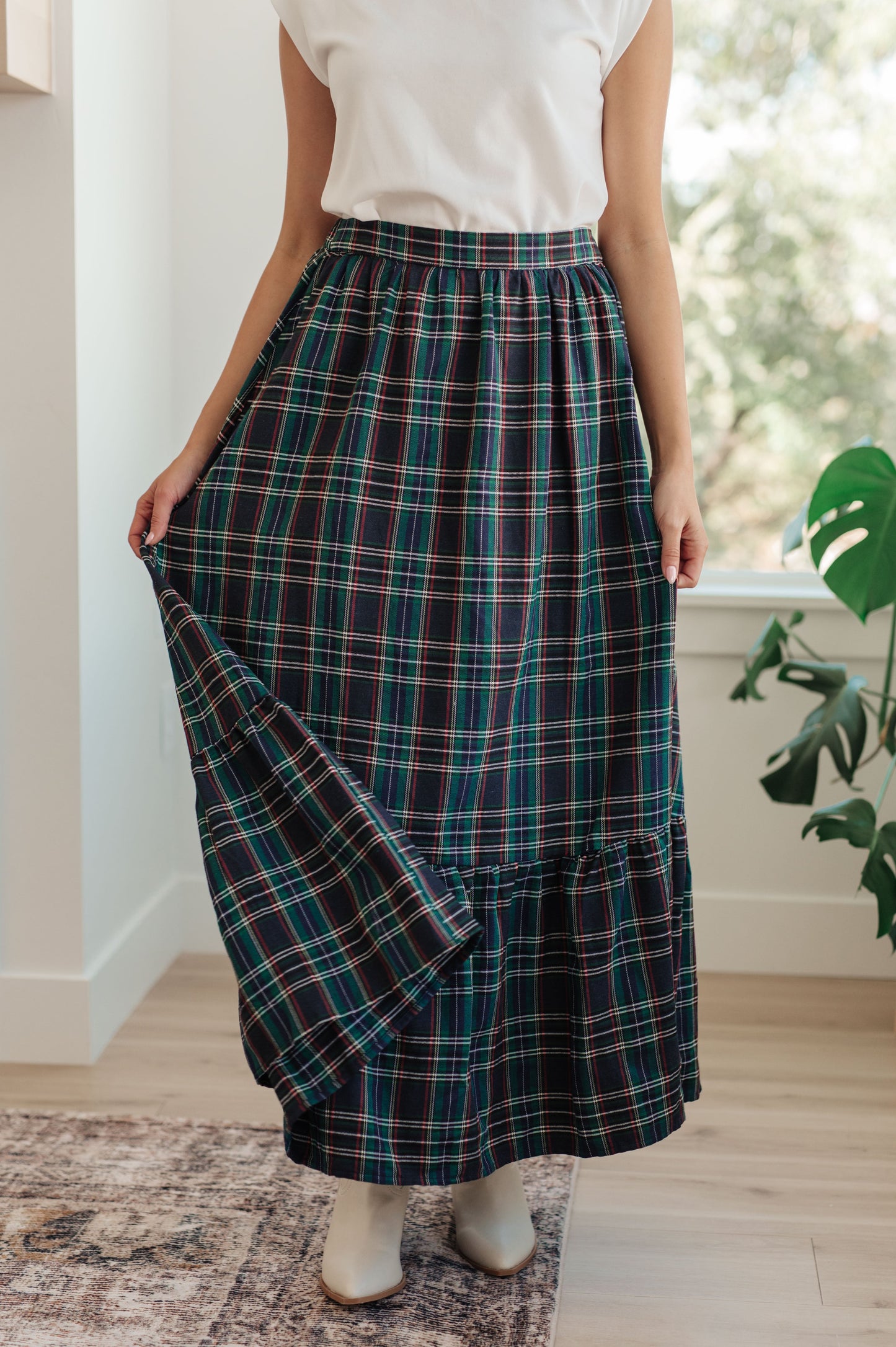 Person wearing a plaid skirt in a home setting with a plant in the background
