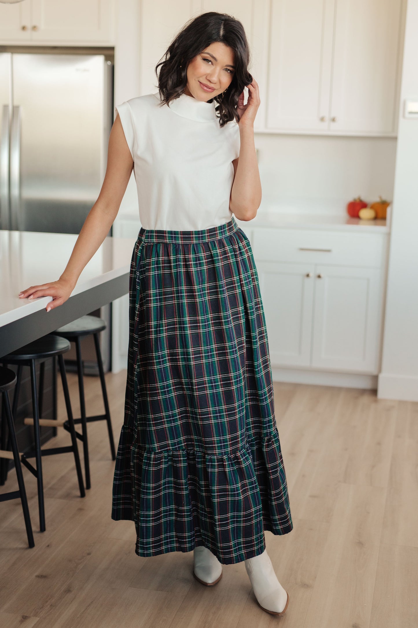 Woman in a kitchen wearing a white top and plaid skirt.