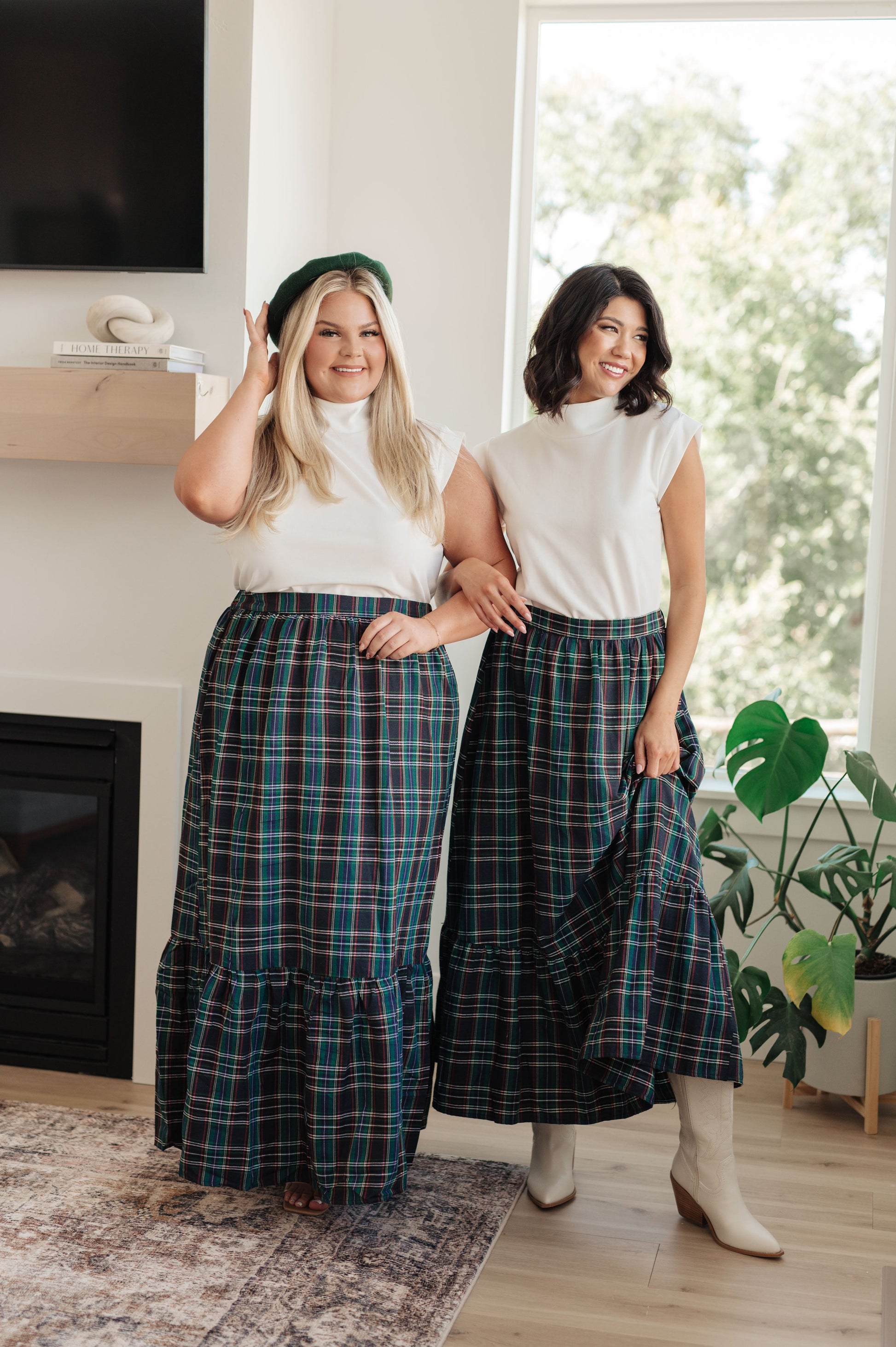Two women wearing matching plaid skirts in a home setting.