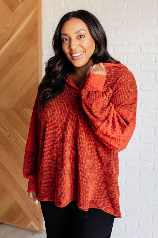 Woman wearing a red sweater standing against a white brick wall.