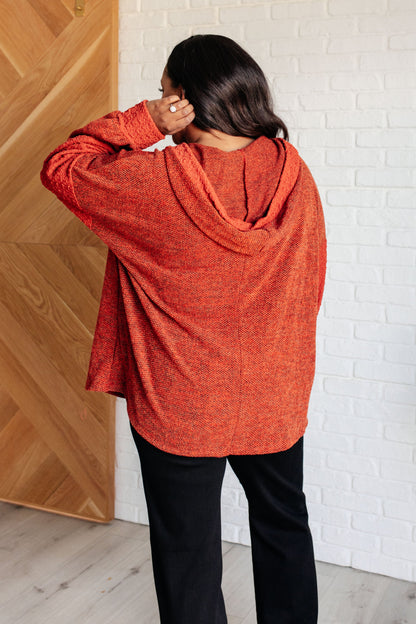 Person wearing an orange hoodie standing against a white brick wall.