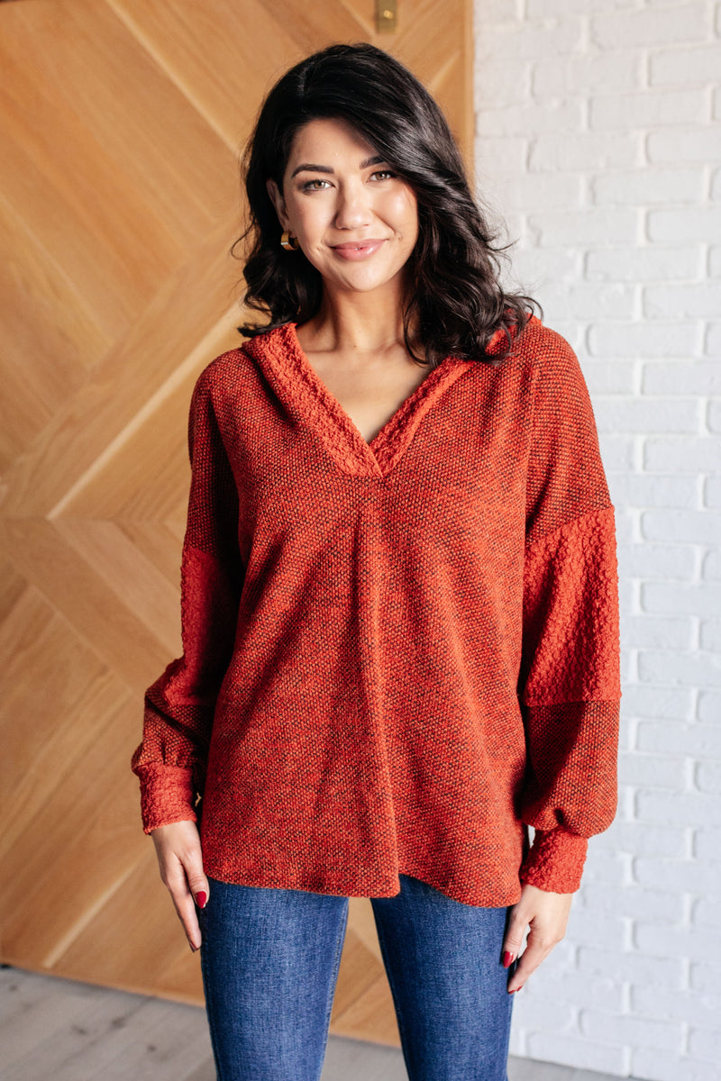 Woman wearing a red sweater standing against a wooden and white brick wall.