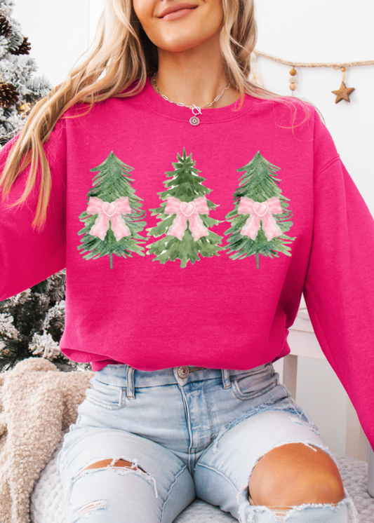 Person wearing a pink sweatshirt with Christmas tree designs in front of a decorated Christmas tree.