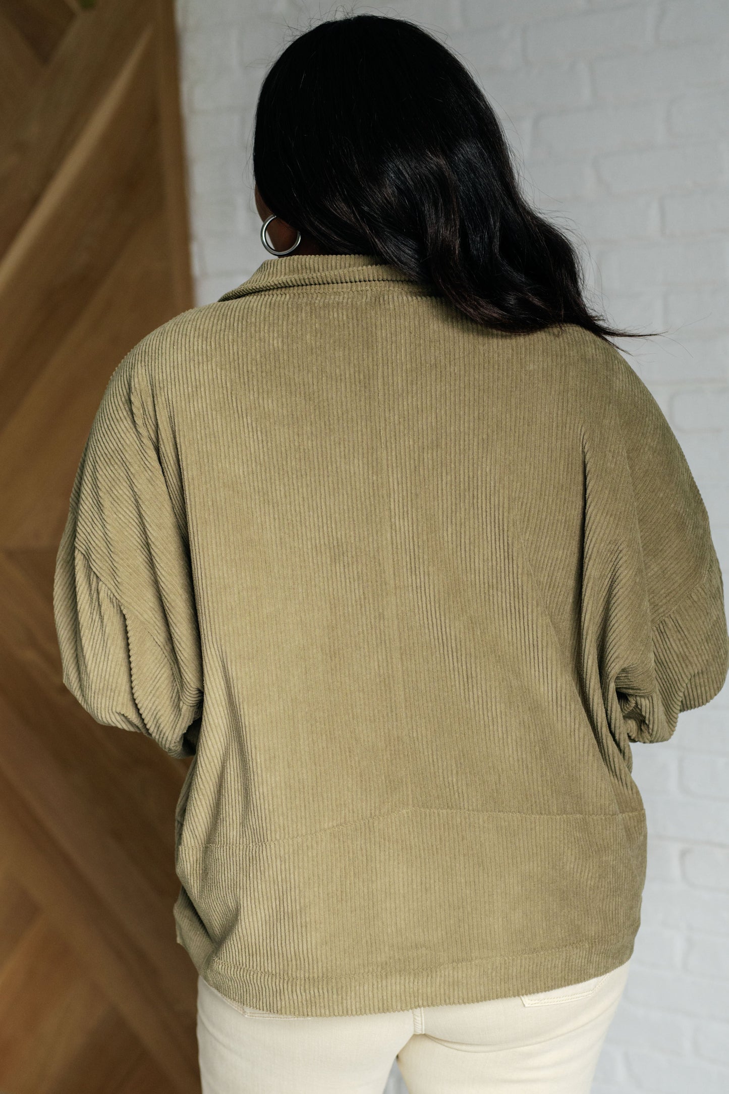 Person wearing a green corduroy jacket with a white brick wall background