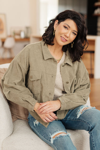 Woman wearing a green jacket and ripped jeans sitting on a couch in a living room.