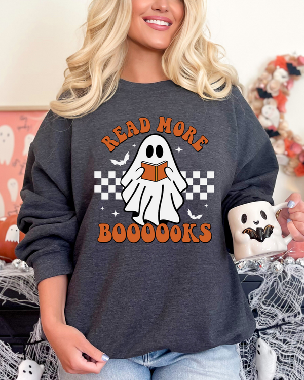 Person wearing a dark gray sweatshirt with a ghost graphic and text, holding a mug in a Halloween-themed setting.