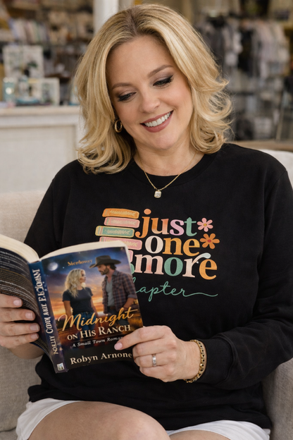Woman reading a book wearing a black sweatshirt with colorful text.