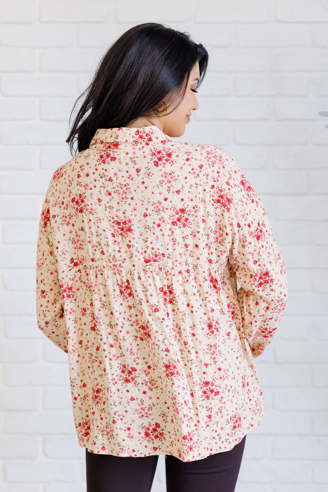 Woman wearing a floral blouse against a white brick wall