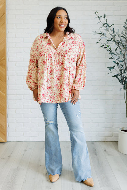 Woman wearing a floral blouse and jeans standing in a room with a white brick wall and plant.