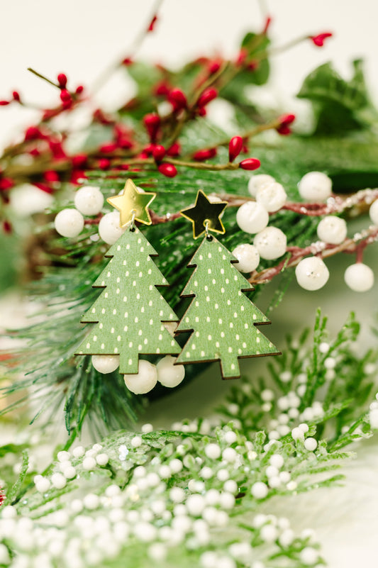 Green Christmas tree earrings on a decorative background with berries and greenery