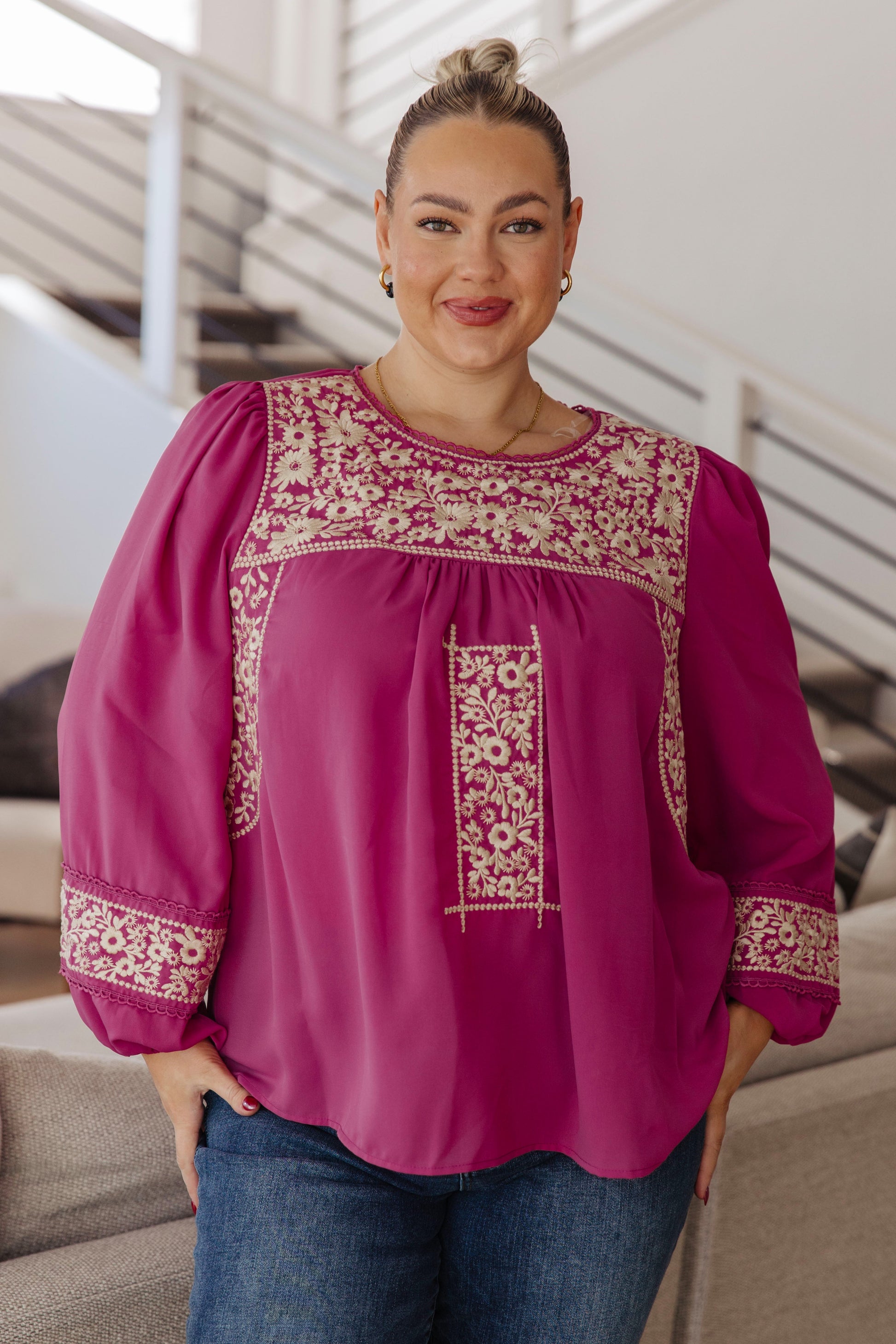 Woman wearing a pink blouse with intricate embroidery in an indoor setting