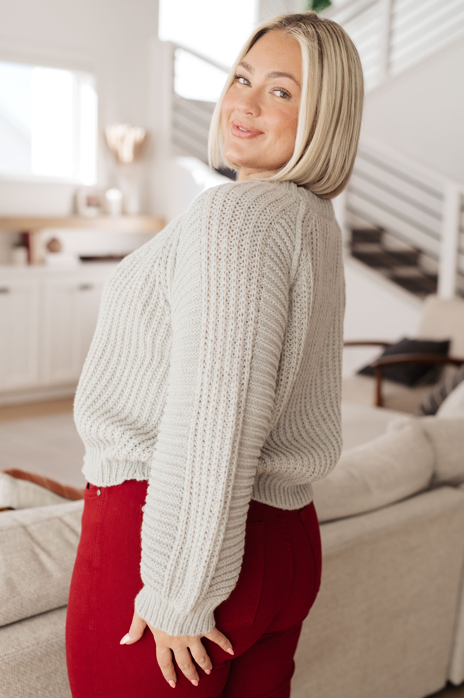 Woman wearing a chunky knit sweater and red pants in a living room setting
