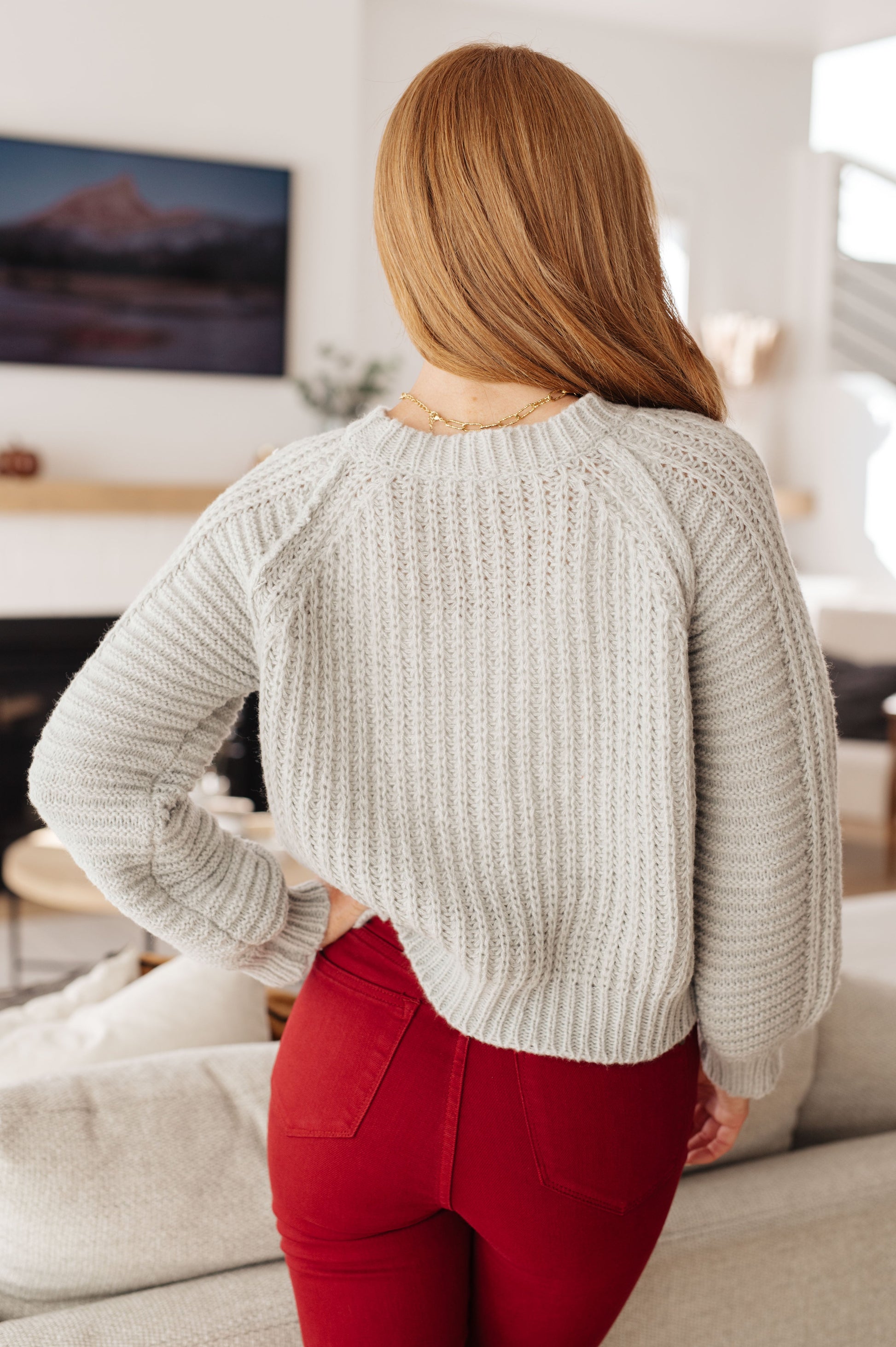 Person wearing a light gray sweater and red pants in a living room setting