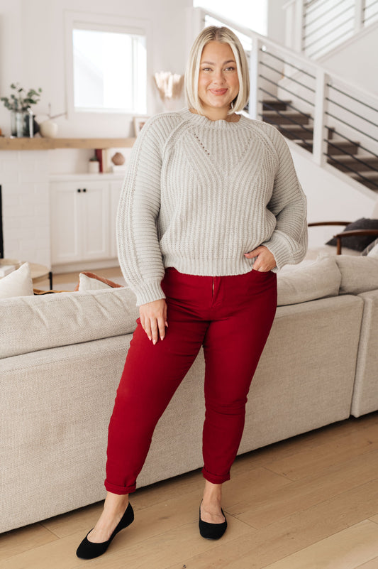 Woman wearing a gray sweater and red pants standing in a living room.