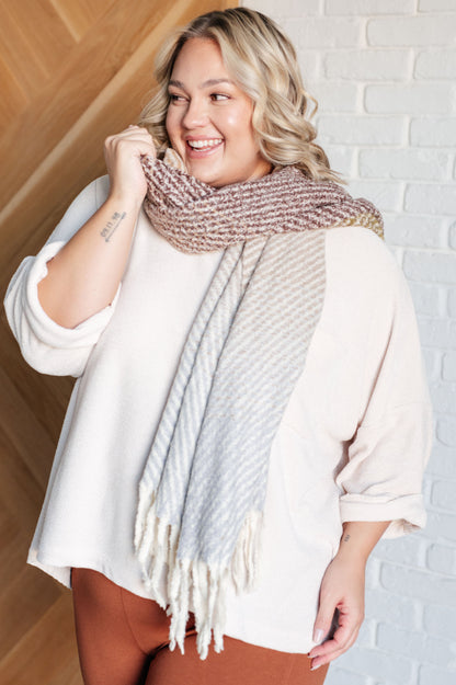 Woman wearing a large, multicolored scarf against a white brick wall.