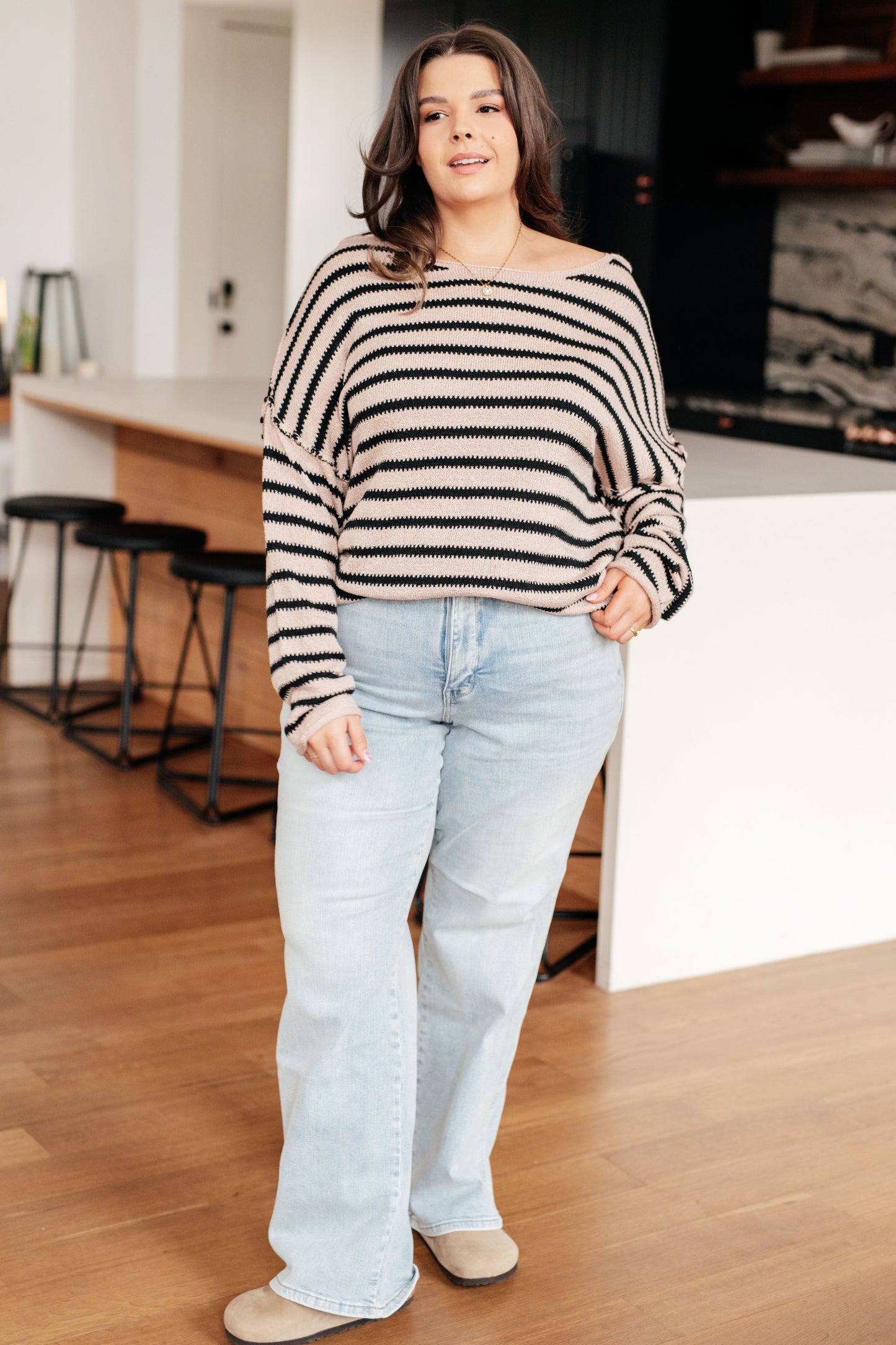 Woman wearing a striped sweater and light blue jeans standing in a kitchen.