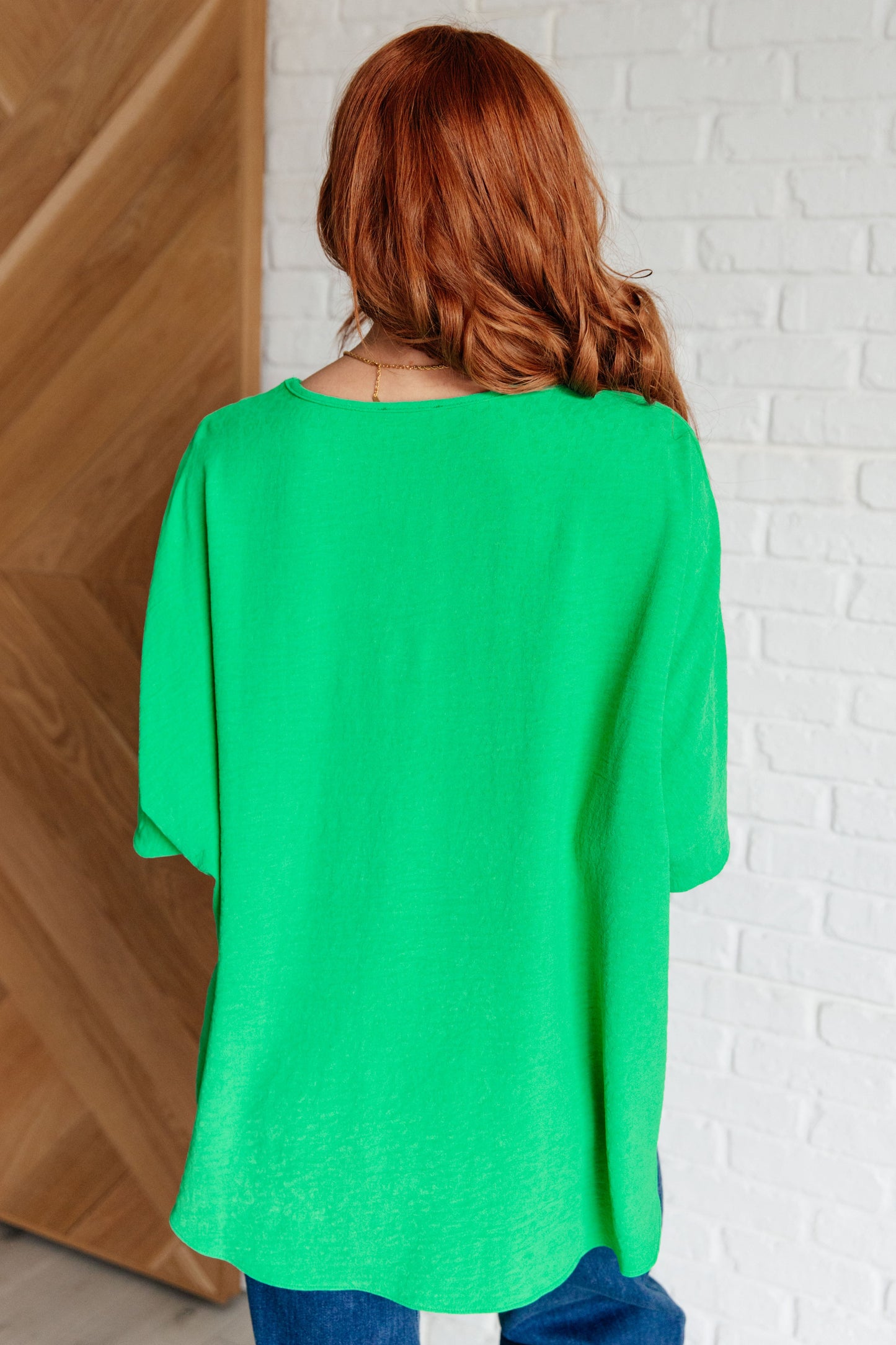 Person wearing a green top with a white brick wall background
