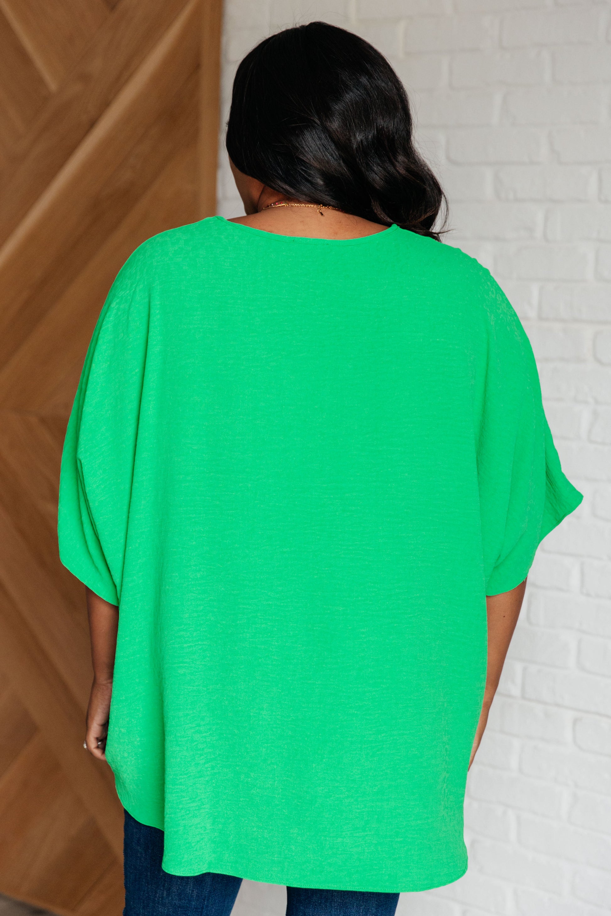 Person wearing a bright green oversized shirt against a white brick wall.