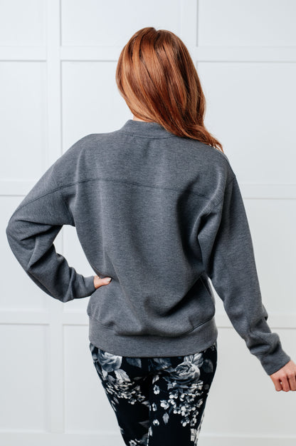 Person wearing a gray sweatshirt with floral leggings against a white tiled wall.