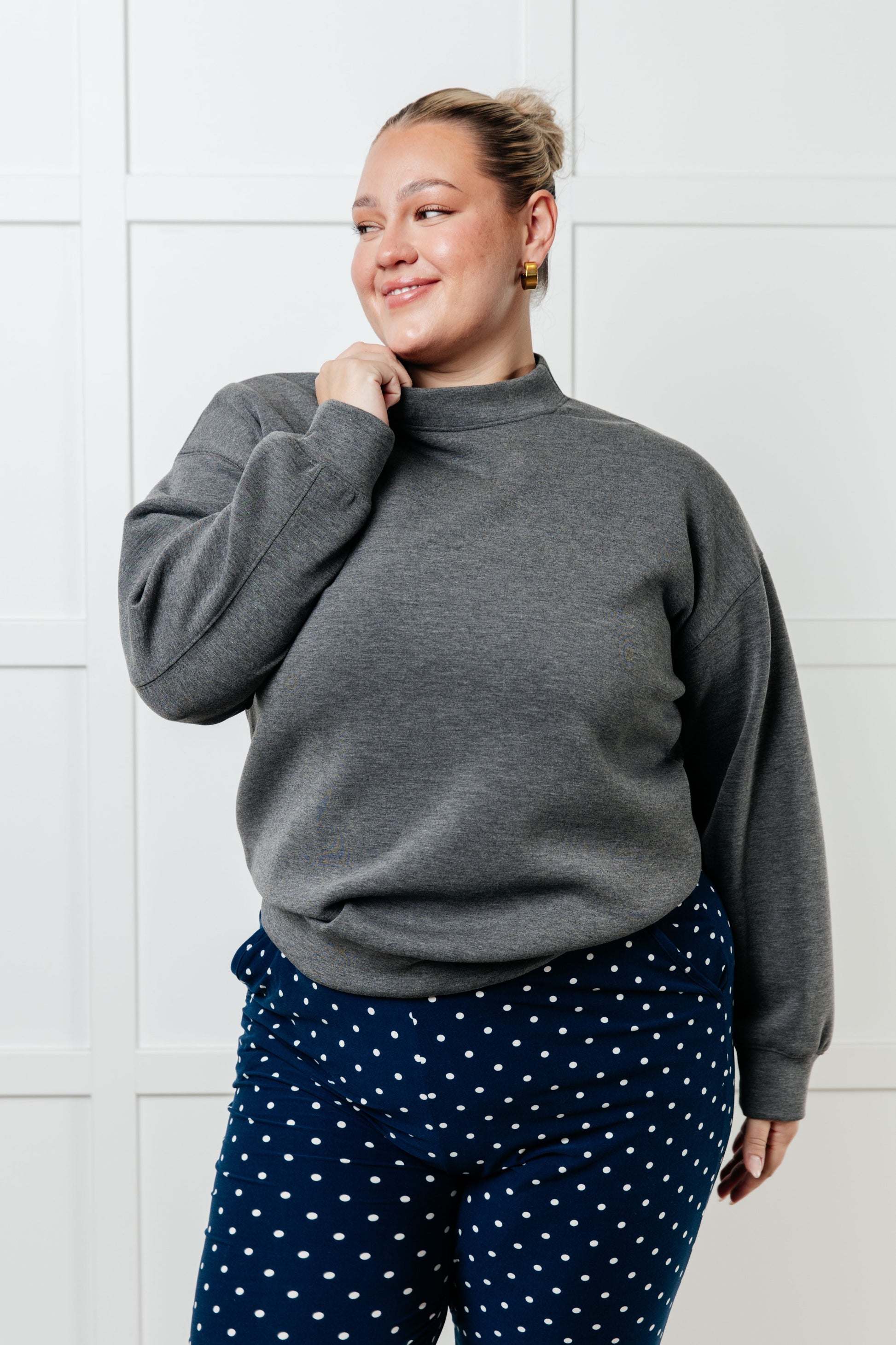 Person wearing a gray sweatshirt and navy polka dot pants against a white wall
