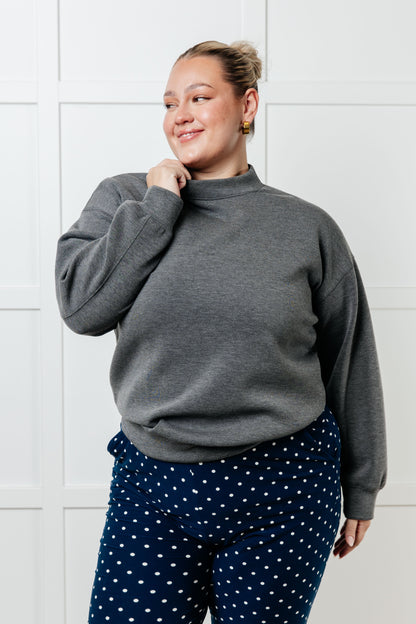 Person wearing a gray sweatshirt and navy polka dot pants against a white wall