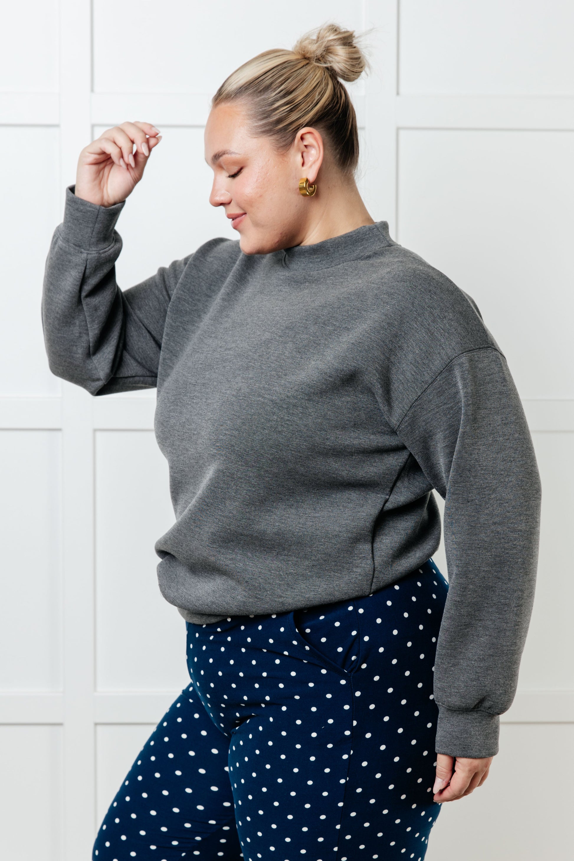 Person wearing a gray sweatshirt and navy polka dot pants against a white tiled wall.