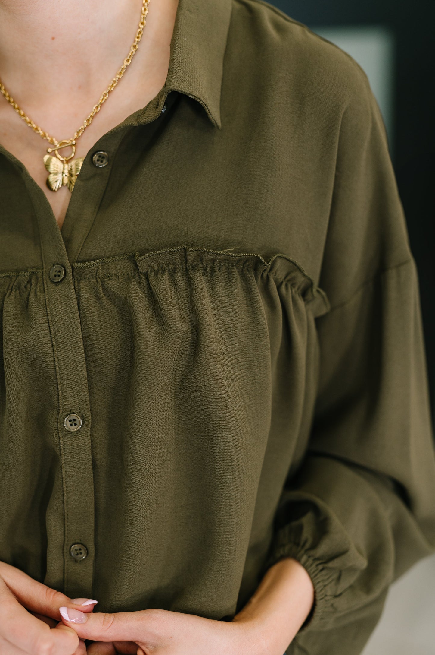Person wearing an olive green button-up shirt with a blurred background