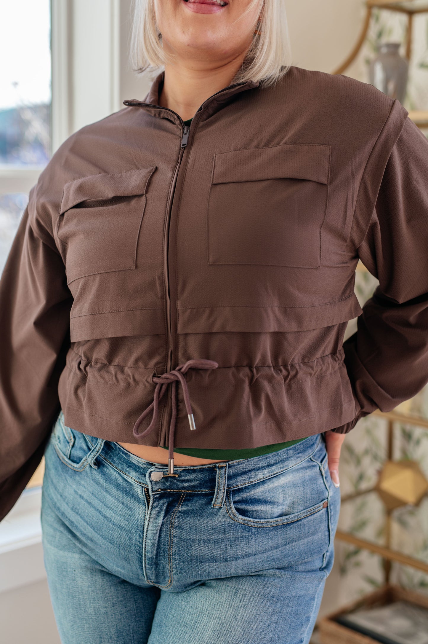 Person wearing a brown jacket and blue jeans indoors