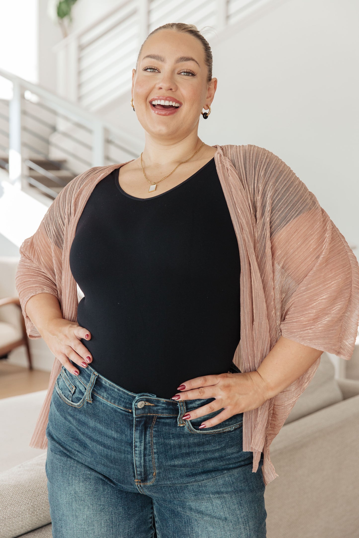 Woman wearing a black top and blue jeans with a pink cardigan in a living room.