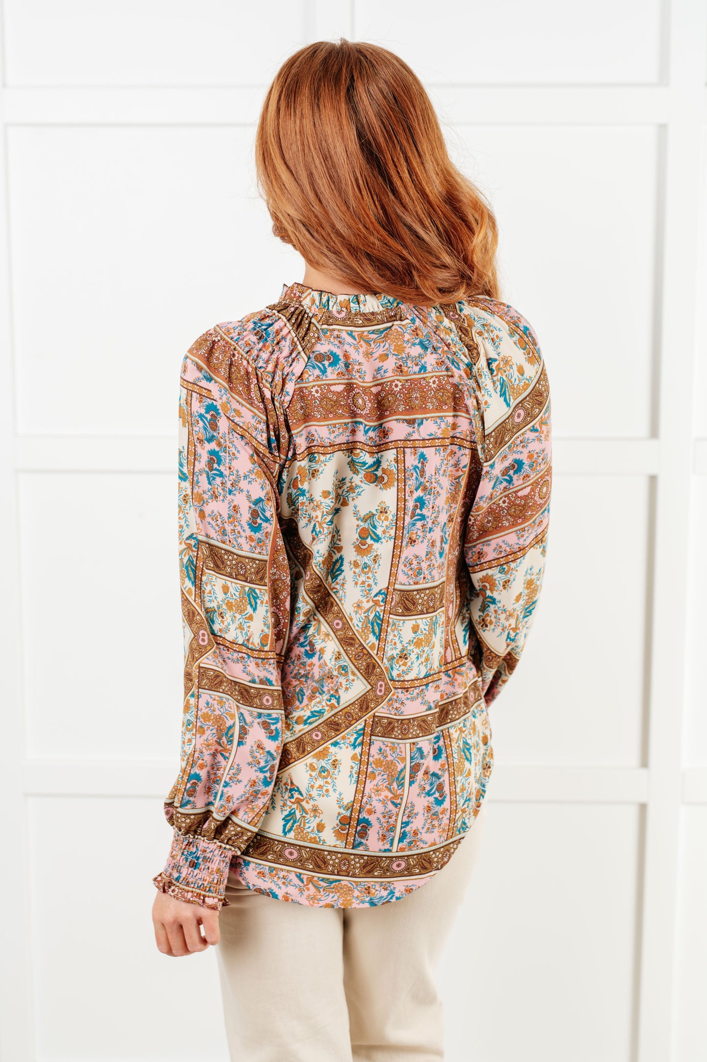 Woman wearing a patterned blouse against a white tiled wall