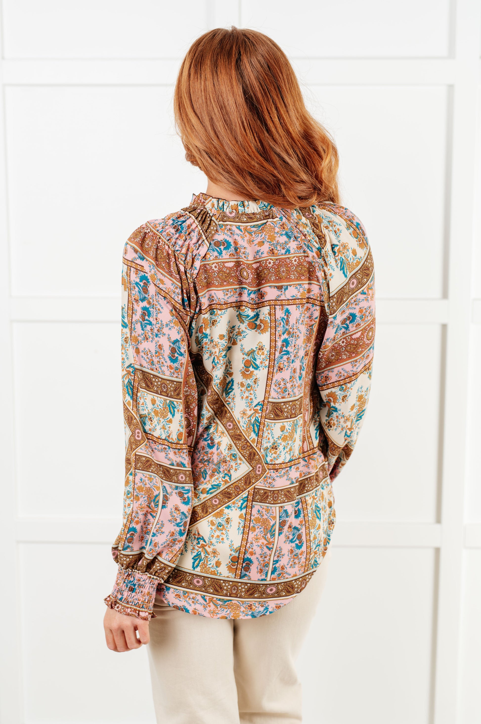 Woman wearing a patterned blouse against a white tiled wall