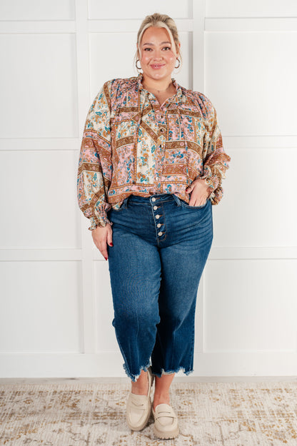 Woman wearing a patterned shirt and blue jeans against a white wall.
