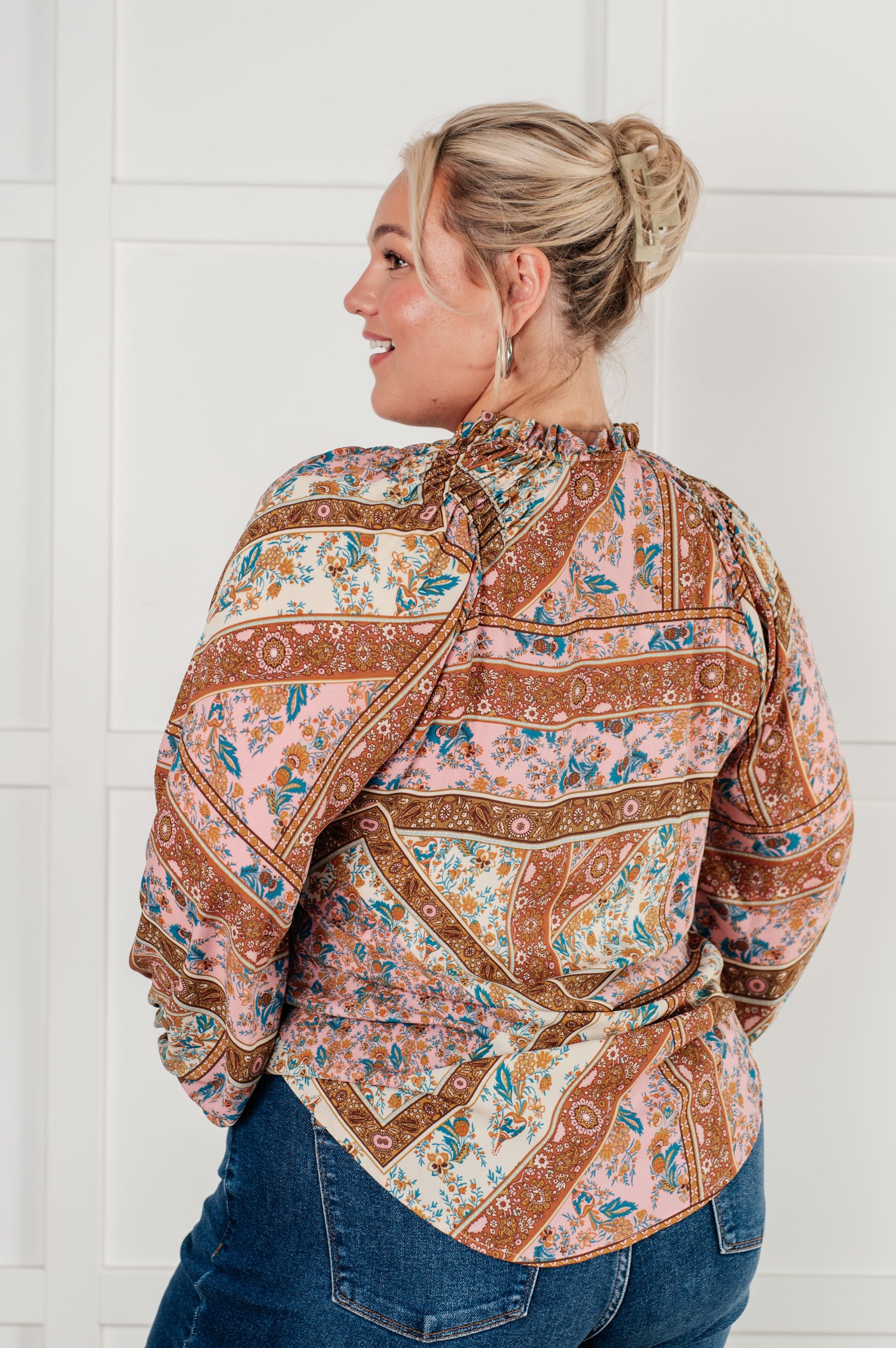 Woman wearing a patterned blouse and jeans against a white wall