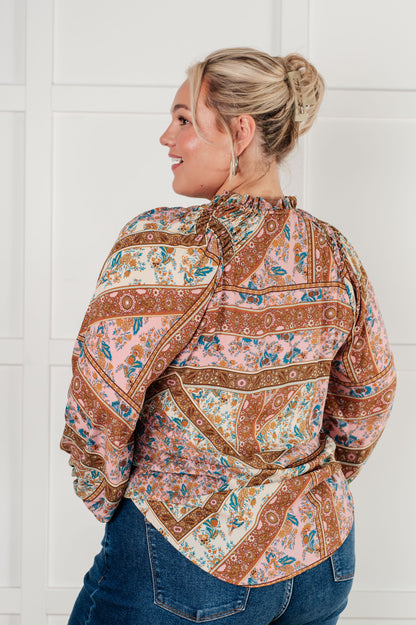 Woman wearing a patterned blouse and jeans against a white wall