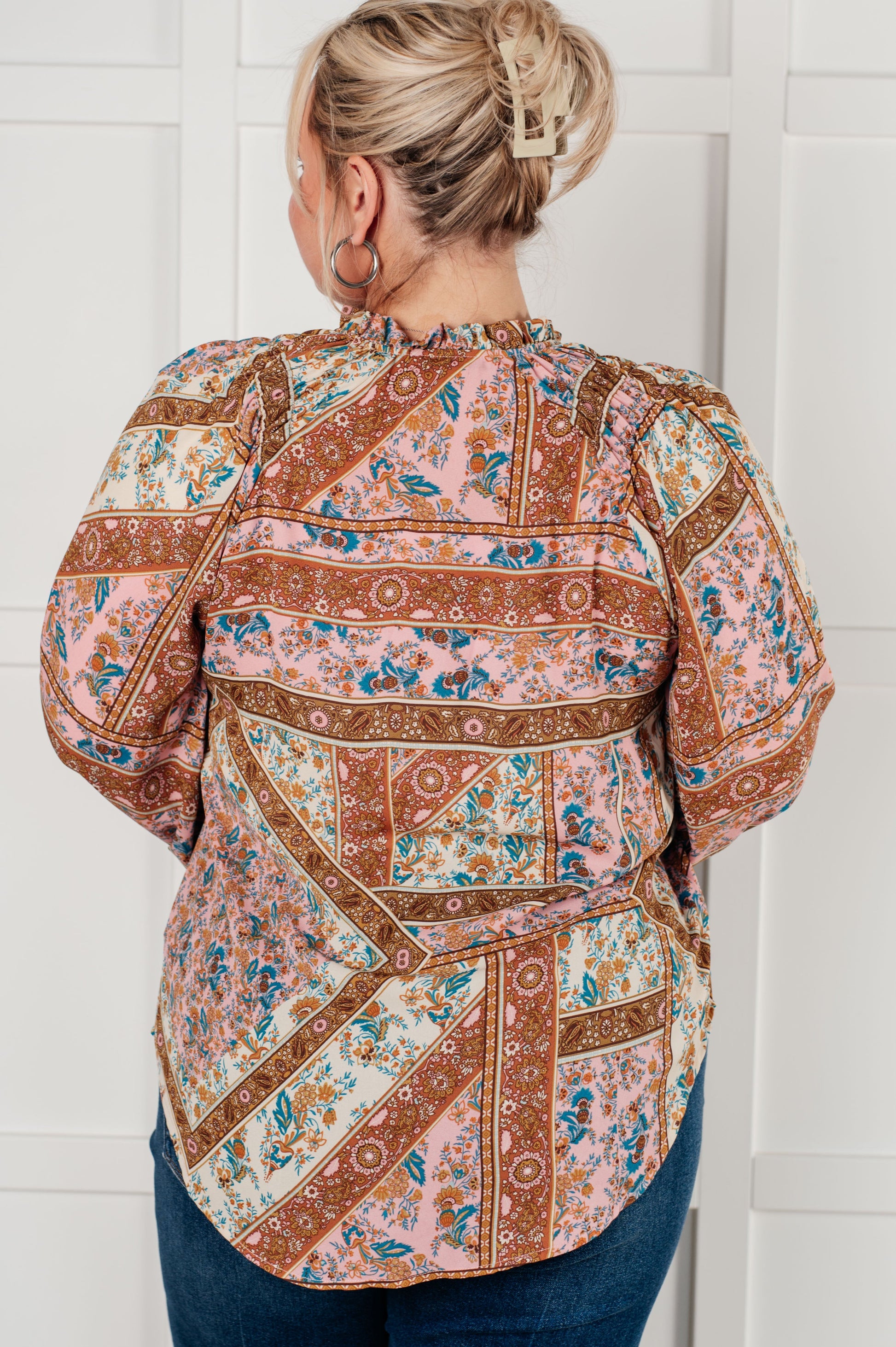 Person wearing a patterned blouse against a white wall
