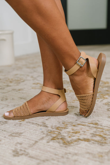 Tan sandals with woven straps worn by a person on a neutral background